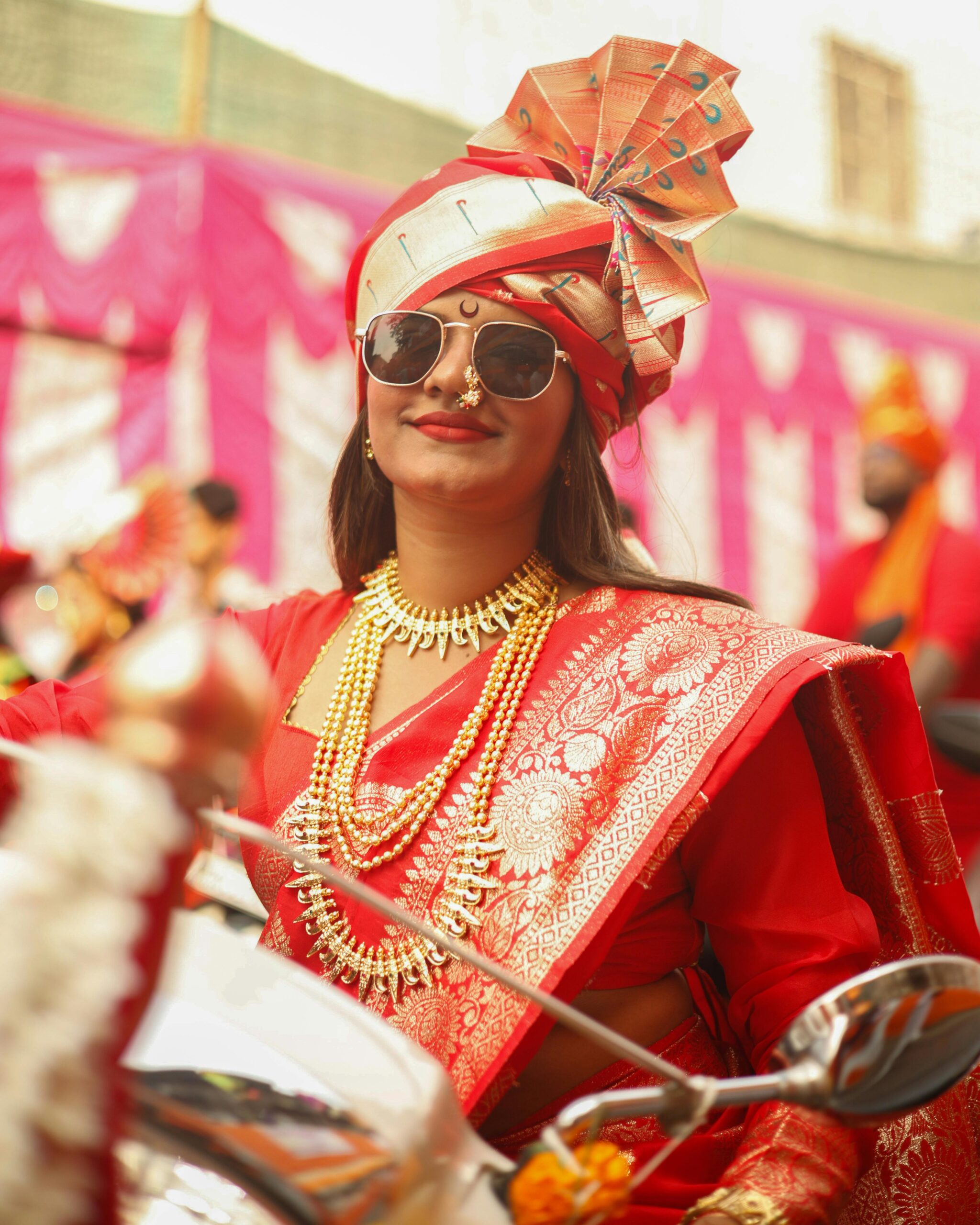 A woman in vibrant Indian traditional attire, adorned with jewelry, partakes in a cultural festival.